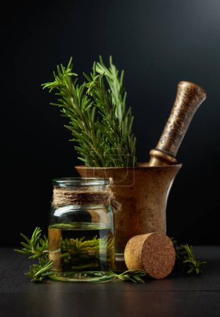 Foto de Botella de extracto de aceite de aromaterapia de romero con ramas de romero fresco y mortero de latón viejo. - Imagen libre de derechos