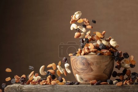 Photo for Flying dried fruits and nuts. The mix of dried nuts and raisins in a wooden bowl. Copy space. - Royalty Free Image