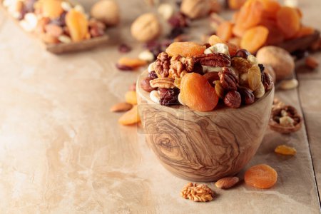 Photo for Dried fruits and nuts on a beige ceramic table. The mix of nuts, apricots, and raisins in a wooden bowl. - Royalty Free Image