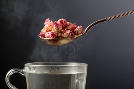 Foto de Brotes de rosa secos para hacer té de hierbas y taza con agua caliente. - Imagen libre de derechos