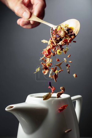 Photo for Mix of dried herbs and flowers is poured into a white teapot. - Royalty Free Image