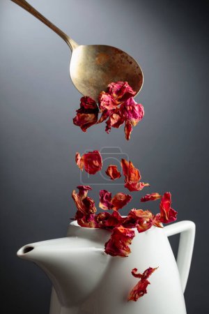 Photo for Dried rose petals are poured into a white teapot. - Royalty Free Image