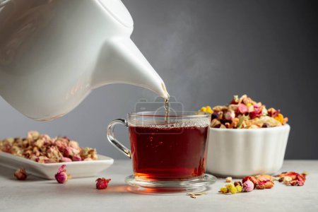 Photo for Herbal tea is poured into a mug. Mixtures of dried herbs and flowers are scattered on the stone table. - Royalty Free Image