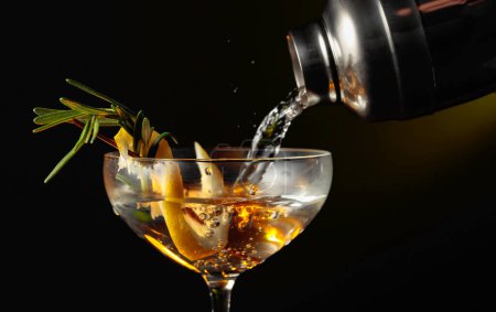 Téléchargez les photos : Gin tonic au romarin et au citron. Le cocktail est versé d'un shaker dans un verre. - en image libre de droit