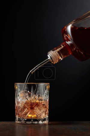Photo for Whiskey is poured from a bottle into a glass with ice. - Royalty Free Image