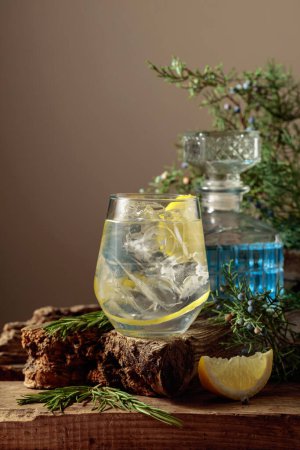 Foto de Cóctel gin-tonic con hielo, limón y romero en un vaso congelado. Una bebida refrescante con ramas de enebro y se engancha en una vieja tabla. Copiar espacio. - Imagen libre de derechos