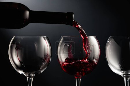 Photo for Pouring red wine into a wine glass on a black background. - Royalty Free Image