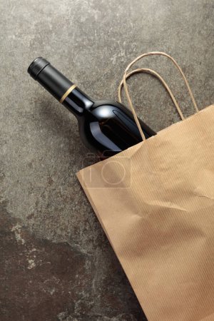 Photo for Paper shopping bag with a bottle of red wine on an old stone background. Top view, copy space. - Royalty Free Image