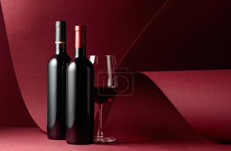 Téléchargez les photos : Bouteilles et verre de vin rouge sur fond rouge. Espace de copie. - en image libre de droit