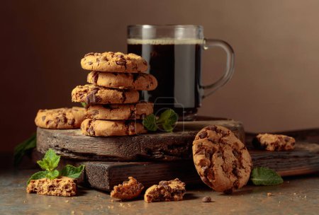 Téléchargez les photos : Freshly baked chocolate cookies with mint and a cup of black coffee on a rustic brown background. - en image libre de droit