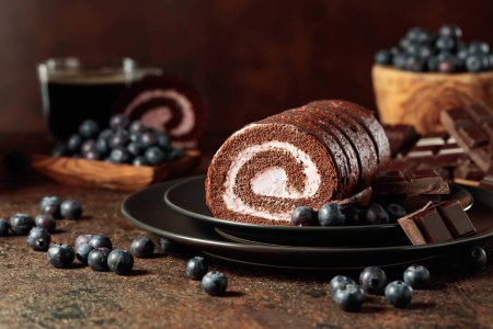 Foto de Pastel de rollo de chocolate con arándanos y una barra de chocolate negro roto. - Imagen libre de derechos