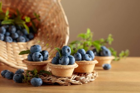 Photo for Small tartlets with fresh blueberries and mint on a wooden table. - Royalty Free Image