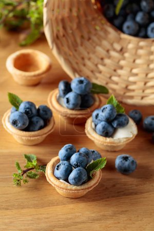 Photo for Small tartlets with fresh blueberries and mint on a wooden table. - Royalty Free Image