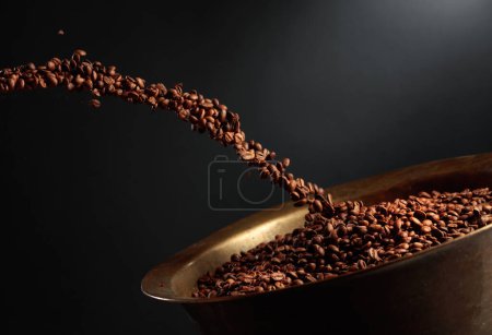 Foto de Medium-roasted coffee beans are poured into an old brass roasting pan. Copy space. - Imagen libre de derechos