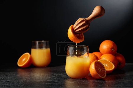 Foto de El jugo de naranja se exprime de la fruta fresca. El jugo se vierte en un vaso con hielo. El concepto de alimento orgánico natural. - Imagen libre de derechos