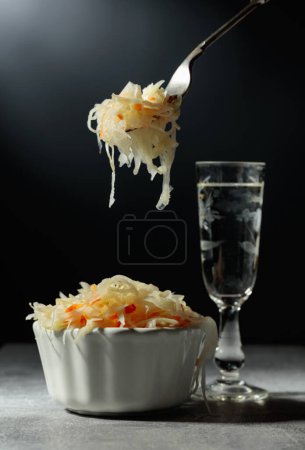 Photo for Bowl of sauerkraut and a glass of vodka on a grey stone table. - Royalty Free Image