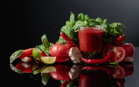 Foto de Salsa de tomate picante con ingredientes. Tomates frescos, pimiento rojo, ajo, albahaca y lima sobre un fondo negro. - Imagen libre de derechos
