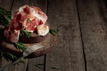 Téléchargez les photos : Prosciutto italien ou jamon espagnol avec romarin sur une vieille table en bois. Espace de copie. - en image libre de droit