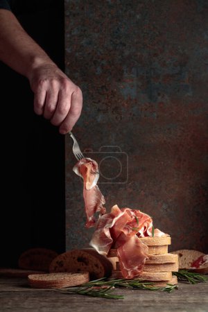 Téléchargez les photos : Prosciutto avec pain et romarin sur un vieux fond rustique. Cuisine méditerranéenne traditionnelle. Espace de copie. - en image libre de droit