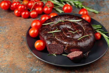 Photo for Black pudding or blood sausage with rosemary and tomatoes on a black plate. - Royalty Free Image