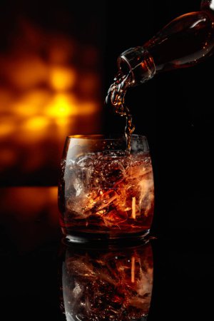 Téléchargez les photos : Verser le whisky d'une bouteille dans un verre glacé. - en image libre de droit