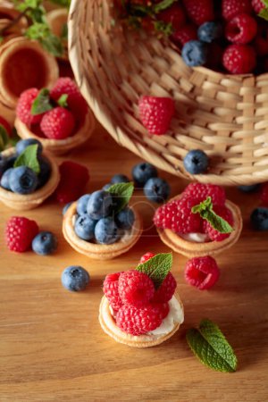 Photo for Small tartlets with fresh raspberries and blueberries garnished with mint on a wooden table. - Royalty Free Image