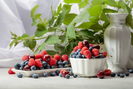 Photo for Berries with leaves on a white table. Colorful assorted mix of blueberries, raspberries, and sweet cherries. - Royalty Free Image