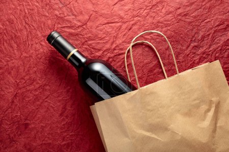 Foto de Bolsa de compras de papel con una botella de vino tinto sobre un fondo rojo texturizado. Vista superior, espacio de copia. - Imagen libre de derechos