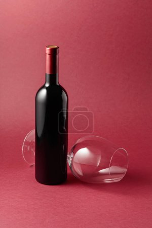 Téléchargez les photos : Bouteille de vin rouge et un verre vide sur fond rouge. Espace de copie. - en image libre de droit