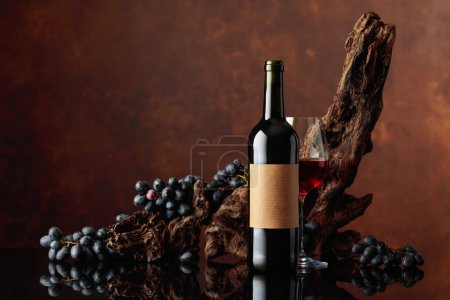 Téléchargez les photos : Bouteille de vin rouge avec vieille étiquette vide. En arrière-plan vieux chicots altérés et raisins bleus. - en image libre de droit