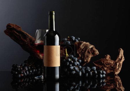 Foto de Botella de vino tinto con etiqueta vieja y vacía. En el fondo viejo enganche envejecido y uvas azules. - Imagen libre de derechos
