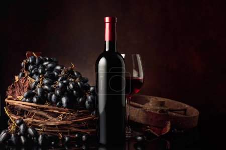Foto de Copa y botella de vino tinto con uvas azules sobre un fondo negro reflectante. Copiar espacio. - Imagen libre de derechos