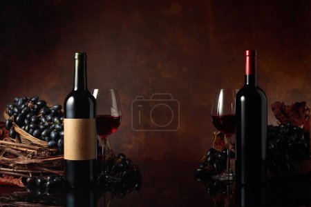 Téléchargez les photos : Bouteilles de vin rouge avec raisins bleus sur fond noir réfléchissant. Espace de copie. - en image libre de droit