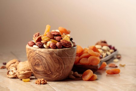 Foto de Dried fruits and nuts on a beige ceramic table. The mix of nuts, apricots, and raisins in a wooden bowl. Copy space. - Imagen libre de derechos