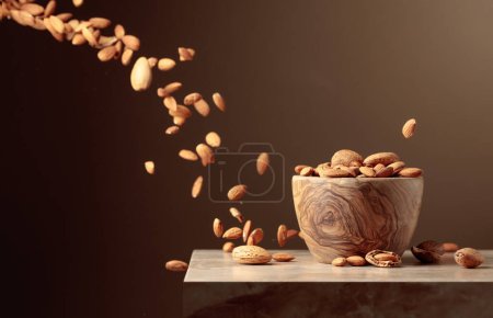 Photo for Almond nuts are poured into a wooden bowl. Brown background with copy space. - Royalty Free Image