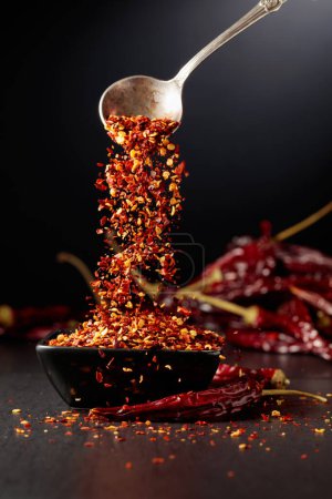 Photo for Chilli flakes are poured into a black dish. Chilli flakes and dried chili peppers on a black background. - Royalty Free Image