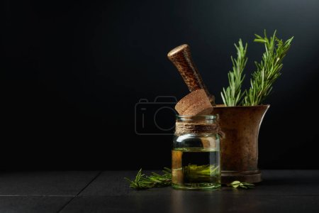 Photo for Bottle of rosemary aromatherapy oil extract with fresh rosemary branches and old brass mortar. Black background with copy space. - Royalty Free Image