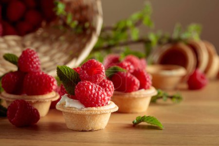 Photo for Small tartlets with fresh raspberries and mint on a wooden table. - Royalty Free Image