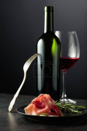 Photo for Prosciutto with rosemary and red wine on a black background. Copy space for your text. - Royalty Free Image