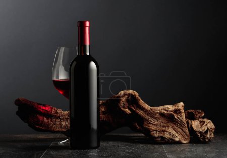 Foto de Botella y copa de vino tinto sobre una mesa de piedra negra. En el fondo viejo enganche resistido. Vista frontal con espacio de copia. - Imagen libre de derechos