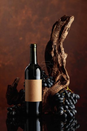 Foto de Botella de vino tinto con la vieja etiqueta vacía. En el fondo viejo enganche envejecido y uvas azules. Copiar espacio. - Imagen libre de derechos