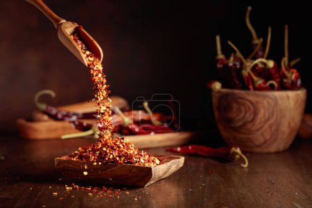 Téléchargez les photos : Les flocons de piment sont versés dans un plat en bois. Flocons de piment et piments secs sur une vieille table en bois. - en image libre de droit