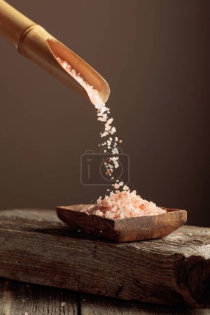 Foto de La sal rosa se vierte con una cuchara de madera en el plato de madera. Copiar espacio. - Imagen libre de derechos