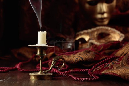 Foto de Bodegón con una vela apagada en un viejo candelero de latón y máscaras de carnaval. - Imagen libre de derechos