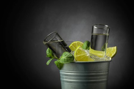 Foto de Bebida alcohólica fuerte con lima y menta en un cubo de metal con hielo. Fondo gris con espacio de copia. - Imagen libre de derechos