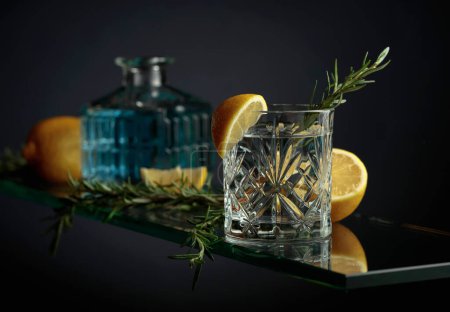 Téléchargez les photos : Boisson rafraîchissante froide au citron et romarin. Cocktail tonique gin dans un verre de cristal. - en image libre de droit