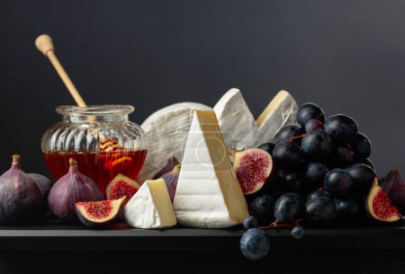 Téléchargez les photos : Fromage camembert aux figues, raisins, noix et miel. Fromage à pâte molle aux fruits sur fond noir. - en image libre de droit