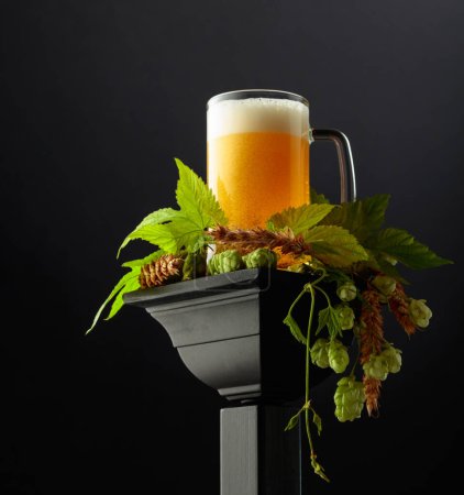 Téléchargez les photos : Tasse de bière avec houblon vert et épis de blé sur un podium noir. Espace de copie. - en image libre de droit