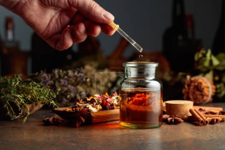 Photo for Dropping essential herbal tincture into a small glass bottle. On a table dried herbs, flowers, spices, and old kitchen utensils. Concept of herbal medicine. - Royalty Free Image