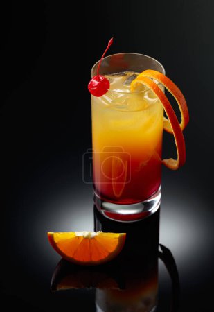 Photo for Cocktail tequila sunrise with a cherry and orange slice on a black reflective background. - Royalty Free Image